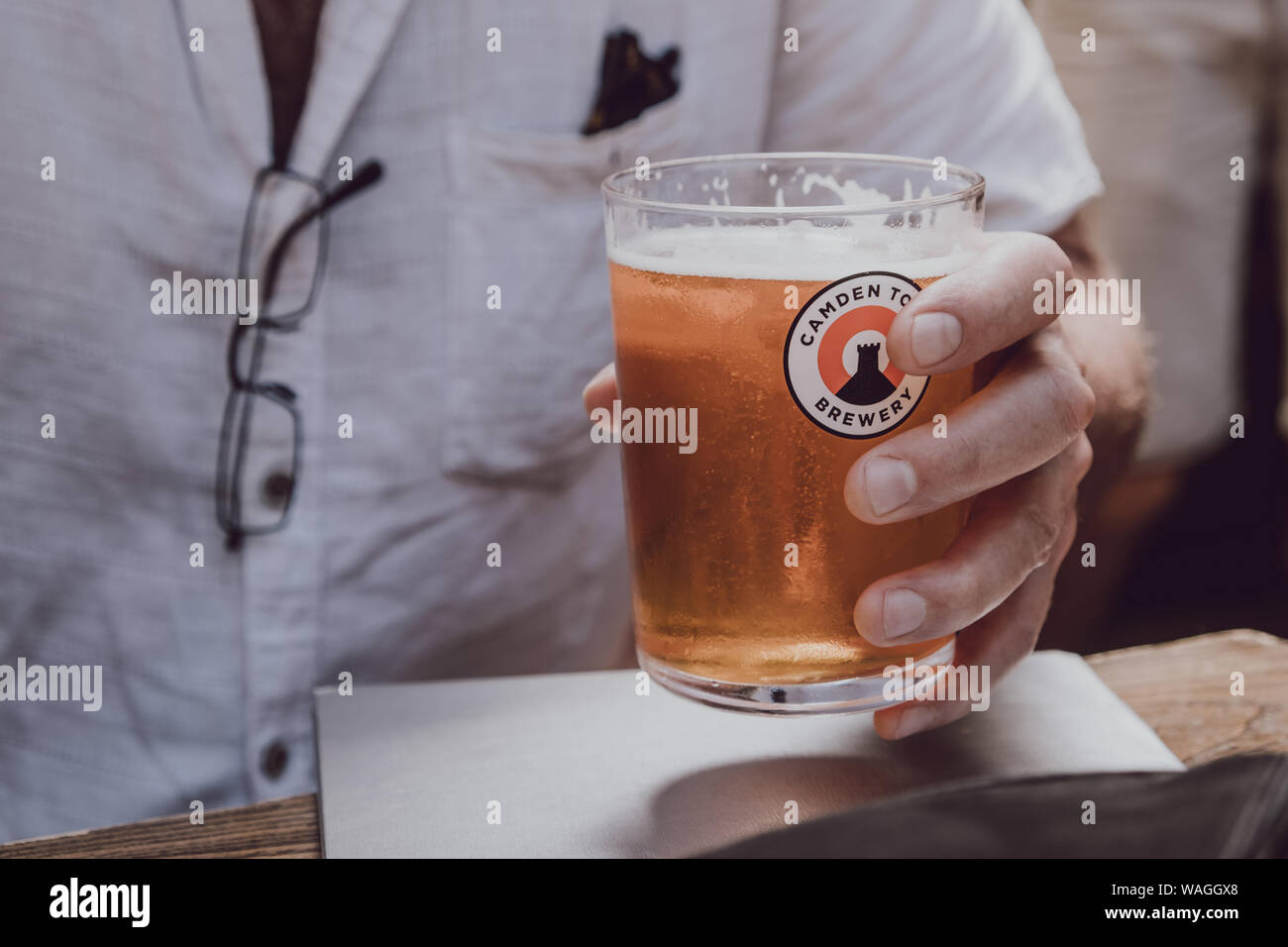 London, Regno Unito - 29 Luglio 2019: l'uomo con in mano un bicchiere di Camden Town Brewery birra. La cittadina di Camden è una londinese brewery fondata nel 2010 specializzata in lag Foto Stock