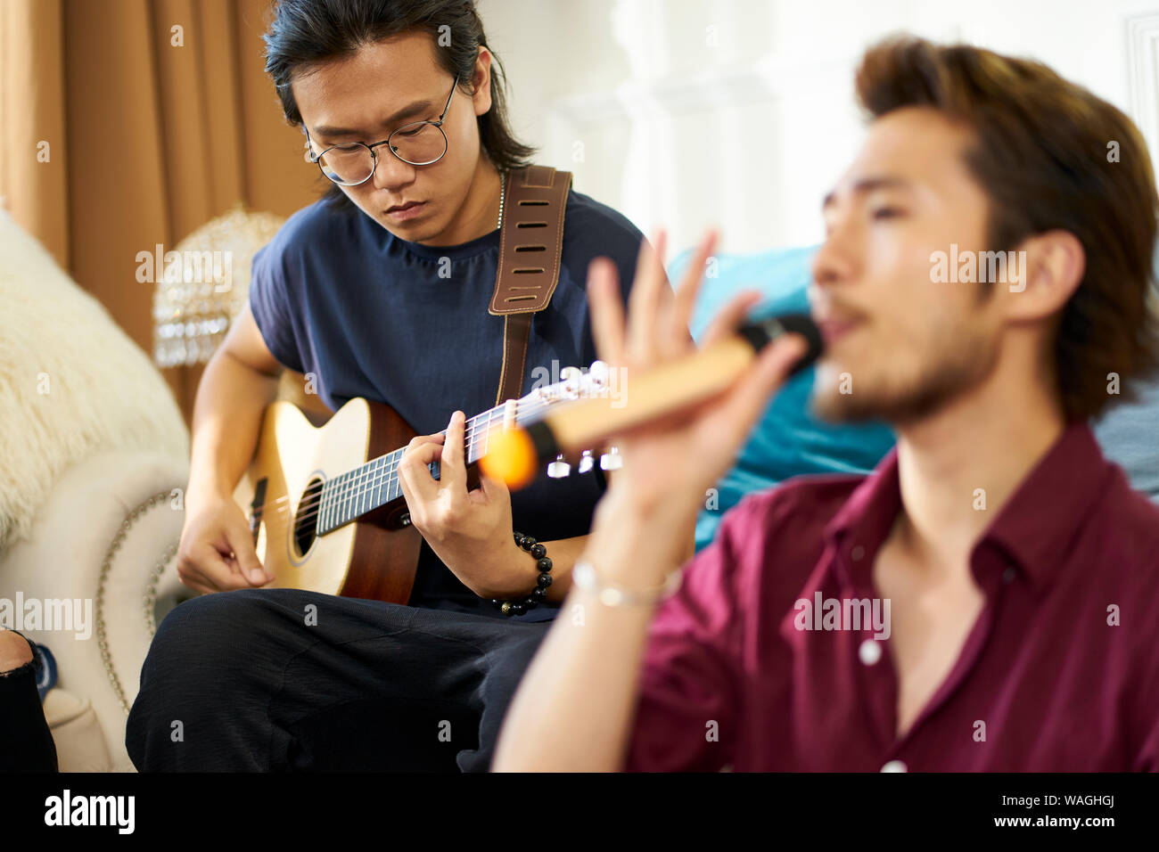 Giovani asiatici uomini adulti rock band membri ripassando cantare suonare strumenti musicali nel salotto di una casa Foto Stock