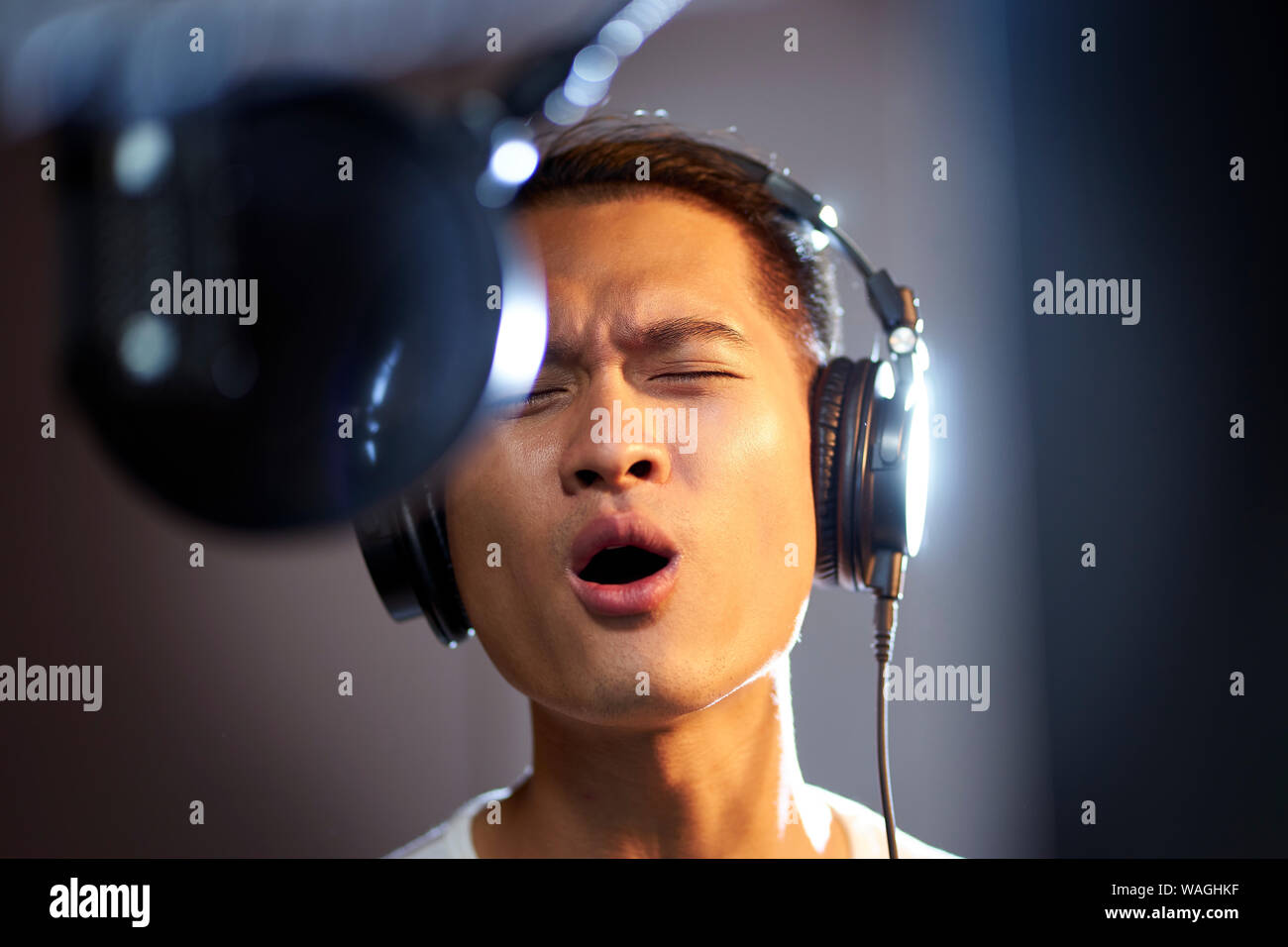Giovani asiatici uomo adulto godendo di cantare una canzone in un moderno studio di registrazione Foto Stock