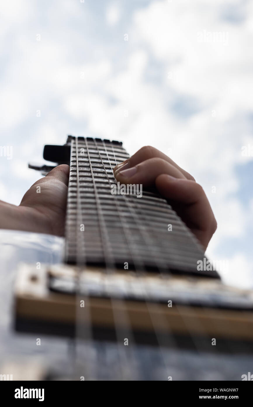Maschio lato suonare la chitarra elettrica e la piegatura delle stringhe con blu cielo nuvoloso in background Foto Stock