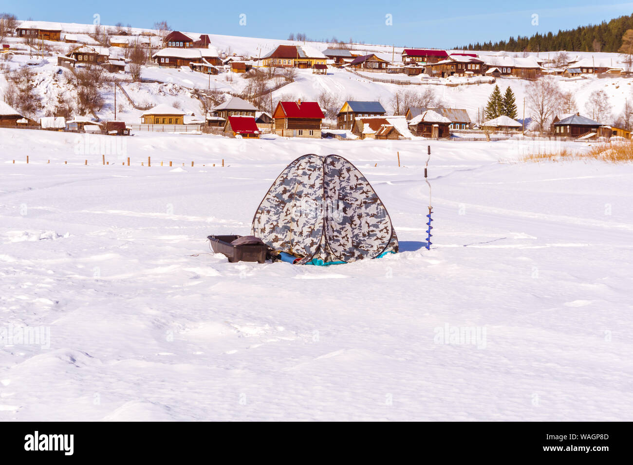 Attrezzature per la pesca sul ghiaccio - tenda-shanty, la coclea a mano e con la slitta - stand sul ghiaccio contro lo sfondo di un inverno paesaggio rurale Foto Stock