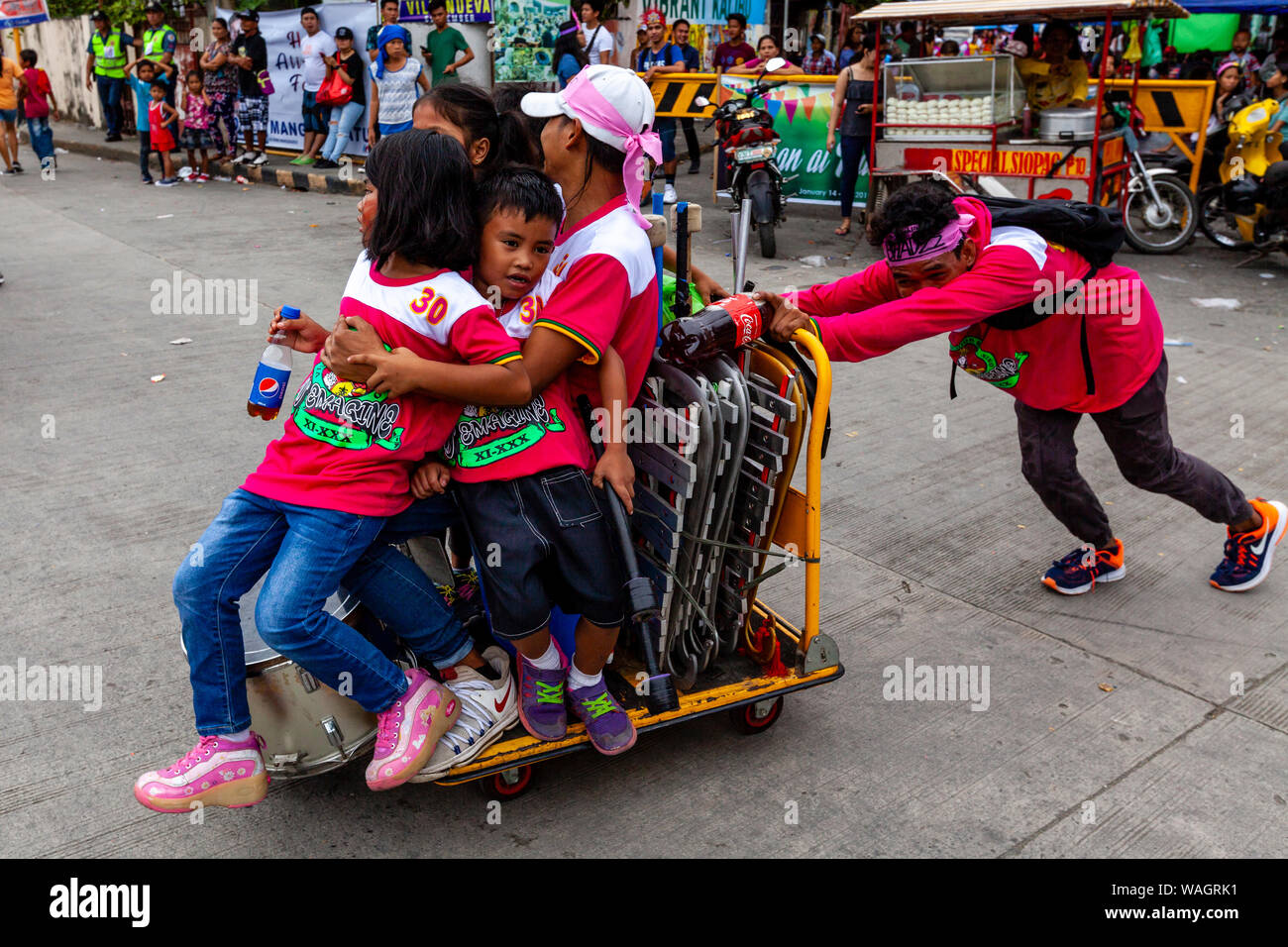 Un giovane uomo spinge un gruppo di bambini in giro su di un carrello, il Festival Ati-Atihan, Kalibo, Panay Island, Aklan Provincia delle Filippine. Foto Stock