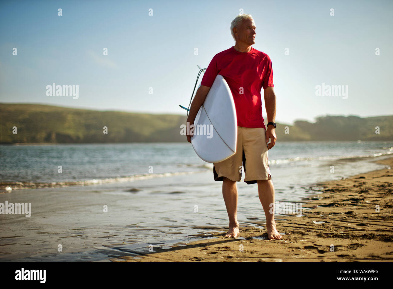 Ritratto di un uomo maturo che porta una tavola da surf su una spiaggia. Foto Stock