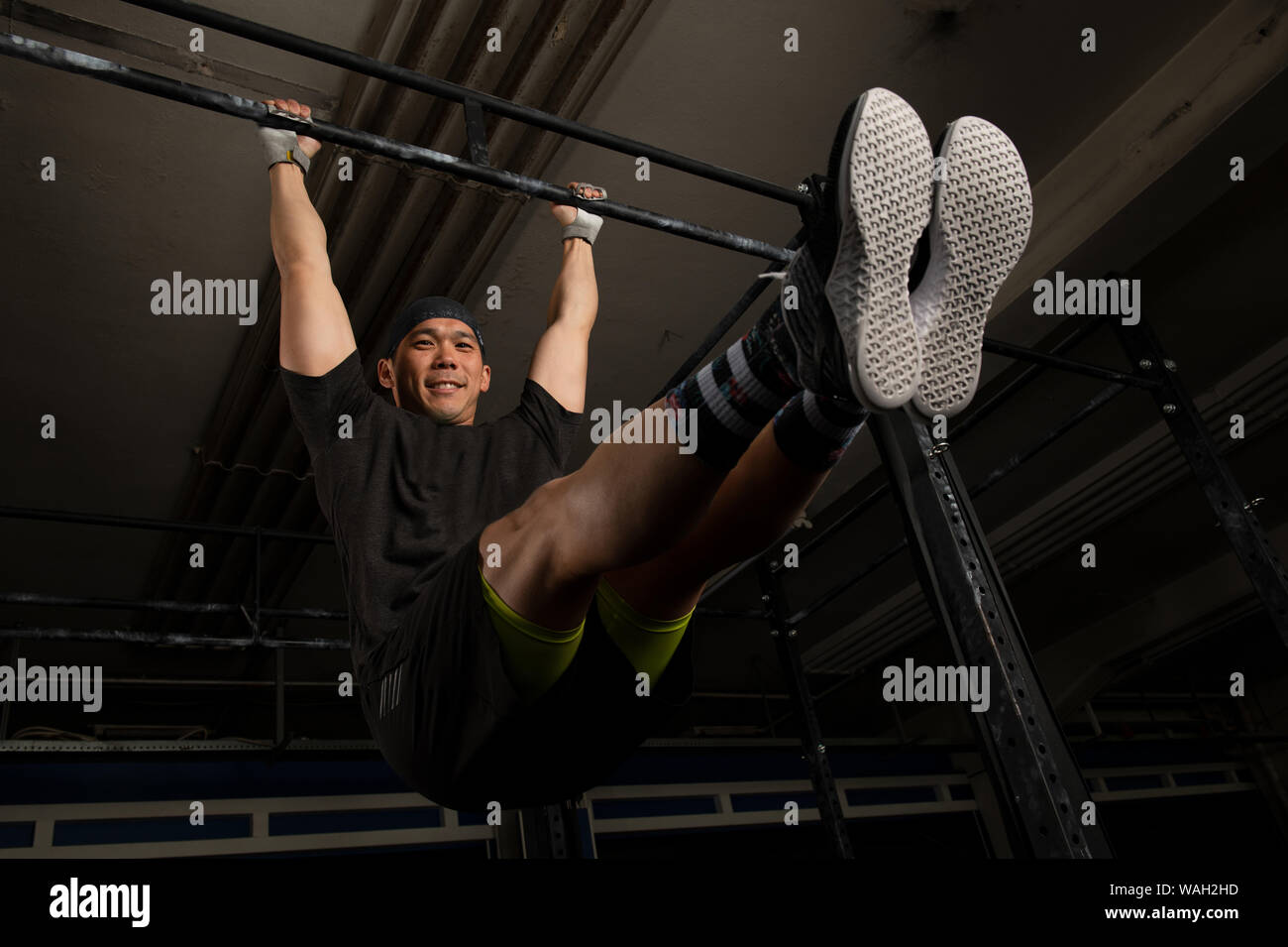 Un bel giovane uomo con muscoli è sorridente e facendo esercizio l sedersi sulla barra orizzontale. Funzionale allenamento fitness in una palestra. Foto Stock