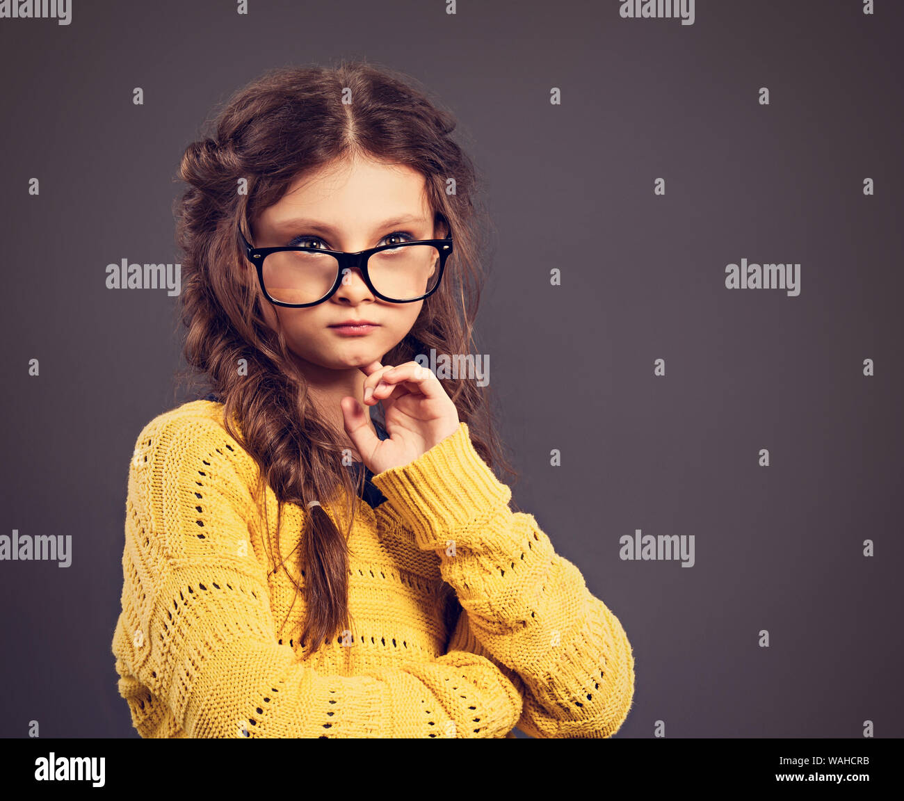 Pensiero serio smorfie schoolgirl in occhiali cercando su grigio di sfondo per studio. Si torna a scuola. Il concetto di istruzione. Closeup tonica colo Foto Stock
