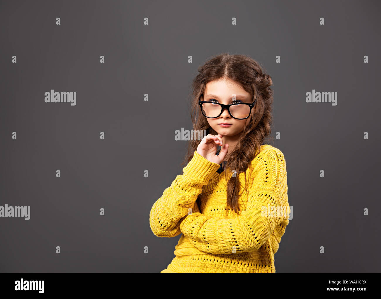 Pensiero serio smorfie schoolgirl in occhiali cercando su grigio di sfondo per studio. Si torna a scuola. Il concetto di istruzione. Closeup ritratto Foto Stock