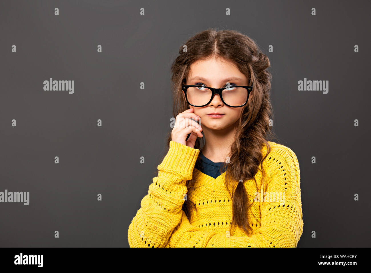 Pensiero serio smorfie schoolgirl in occhiali cercando su grigio di sfondo per studio. Si torna a scuola. Il concetto di istruzione. Primo piano Foto Stock