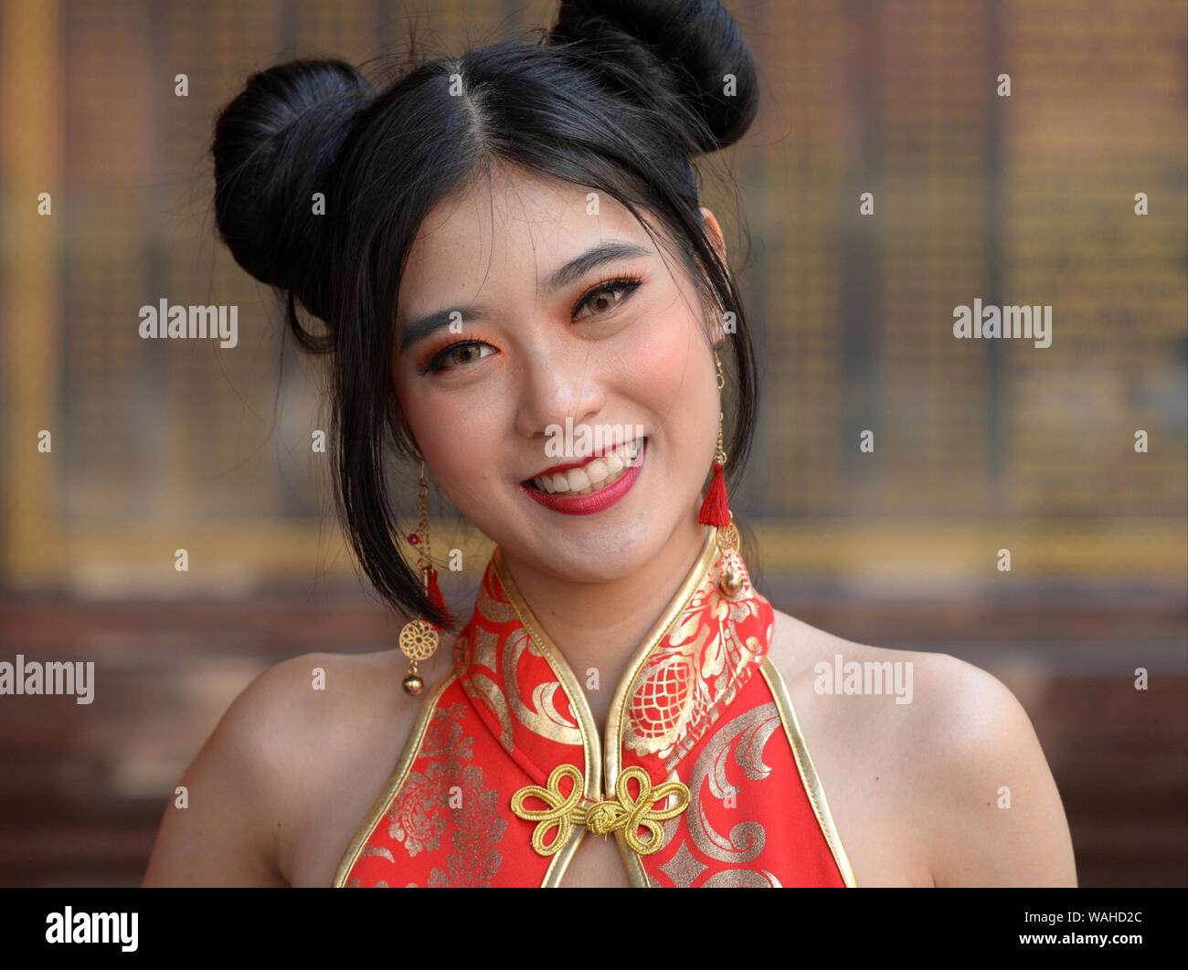 Giovani tailandesi bellezza cinese con Chun Li doppia ciambelle capelli indossa un elegante rosso-oro abito cinese (cheongsam) durante il Capodanno cinese. Foto Stock