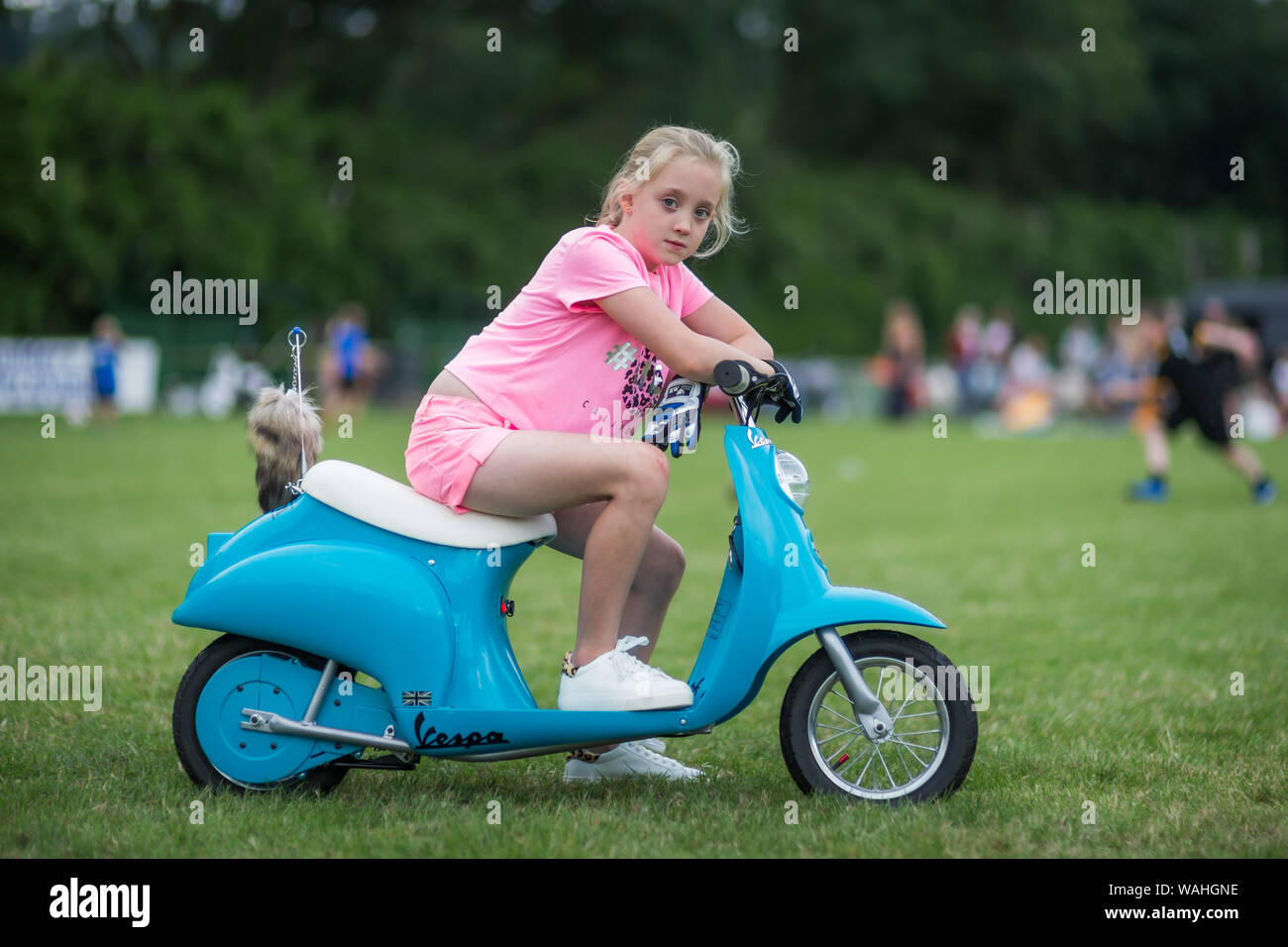 7 anno vecchia ragazza seduta sul suo bambino la dimensione di scooter a motore, REGNO UNITO Foto Stock