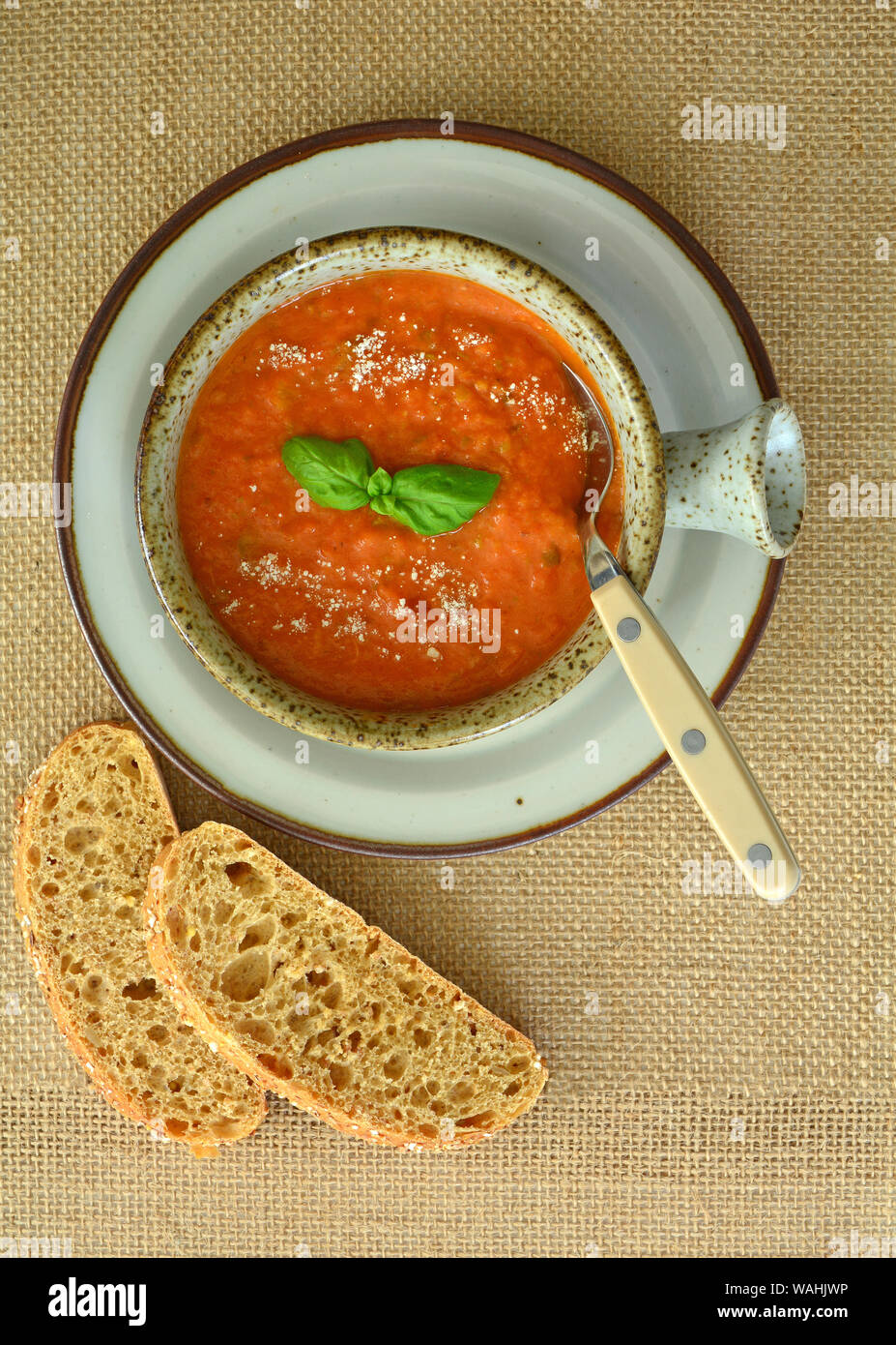 In casa sapido al pomodoro e basilico zuppa nel recipiente rustico con grano intero pane in formato verticale shot dalla testa. Foto Stock