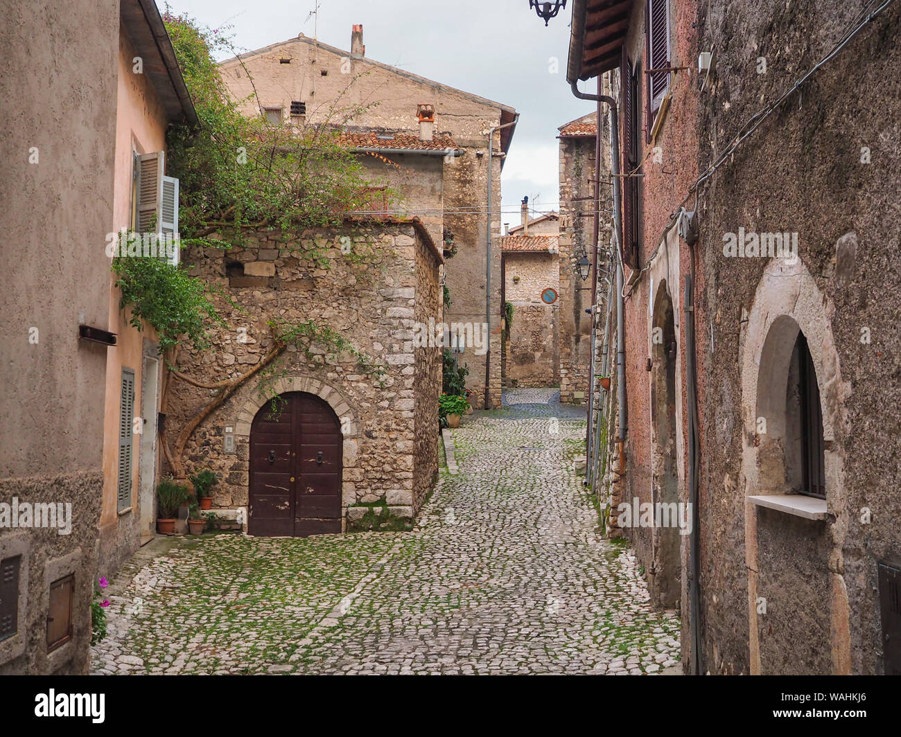 Una pietra di strette strade lastricate e vecchie case medievali con arcate di porte in legno anche metallo tende alle finestre in cittadina antica Sermoneta, Italia Foto Stock