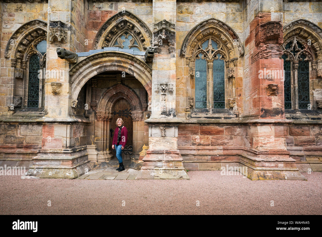 La donna caucasica nel suo 50's sorge nella parte anteriore di una forma ad arco porta in legno presso la Cappella di Rosslyn, Edimburgo, Scozia, Regno Unito, Europa Foto Stock