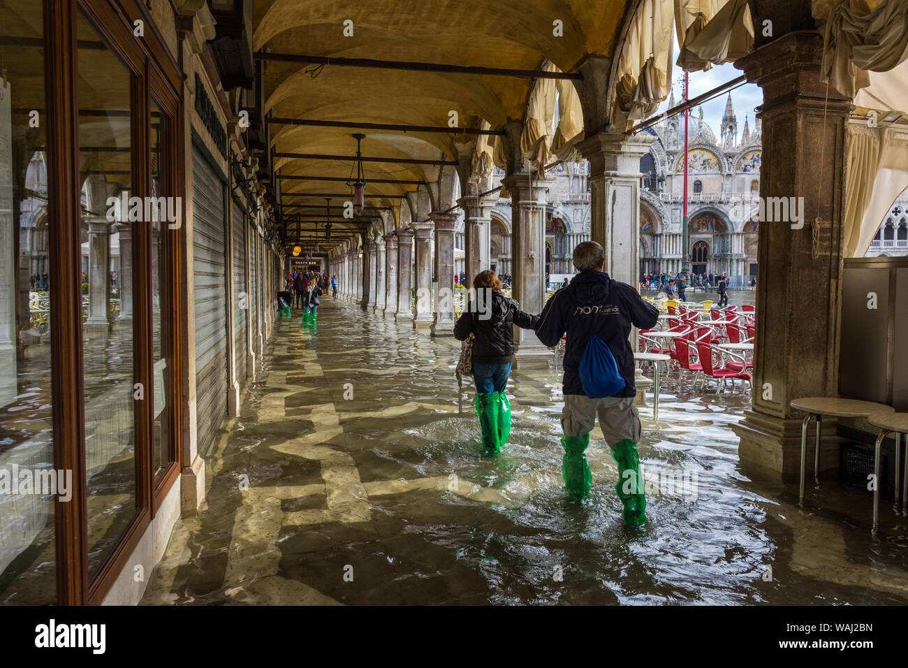 Giovane con soprascarpe impermeabile a portici delle Procuratie Vecchie durante un'acqua alta alta (acqua), eventi di Piazza San Marco, Venezia, Italia Foto Stock