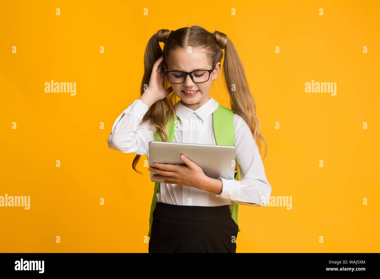 Confuso Schoolgirl utilizzando tavoletta digitale su sfondo giallo Foto Stock
