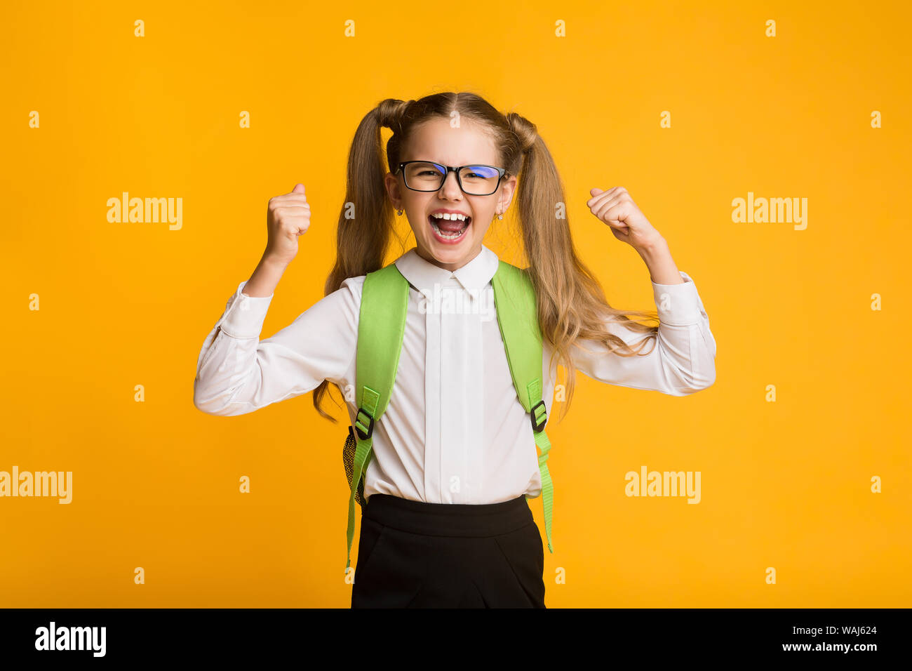Little Schoolgirl Grida gioia la vittoria su sfondo giallo Foto Stock