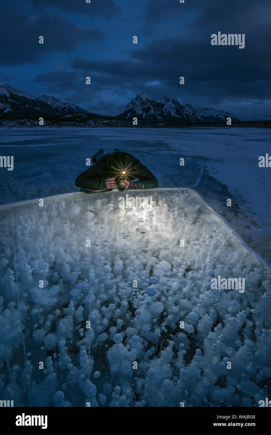 Canada, Alberta, Abramo Lago. Uomo di fotografare le bolle di metano sul lago ghiacciato. (MR) Foto Stock