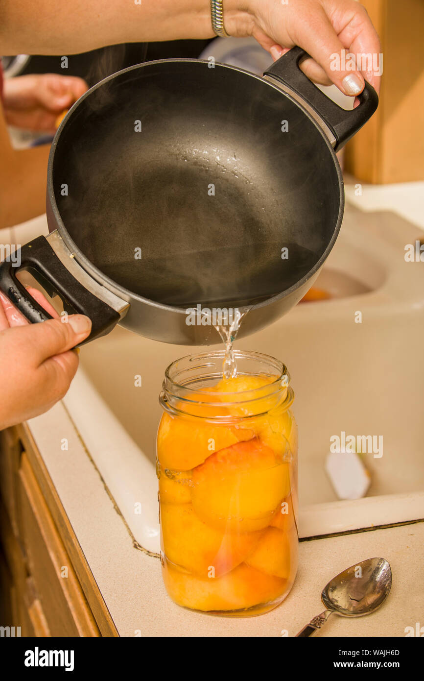 Donna colata di sciroppo caldo miscela (zucchero e acqua miscela) in una giara di mezze pesche fino a quando le pesche sono coperti e pronto per essere inscatolato. (MR) Foto Stock