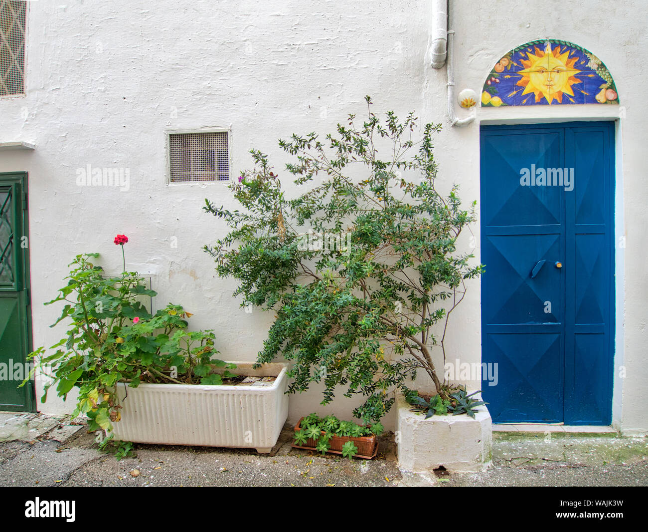 L'Italia, Puglia, Brindisi, Valle d'Itria, Ostuni. Porta blu con colorati sun illustrazione sopra la porta e vasi di piante lungo la parete nella città vecchia di Ostuni. Foto Stock