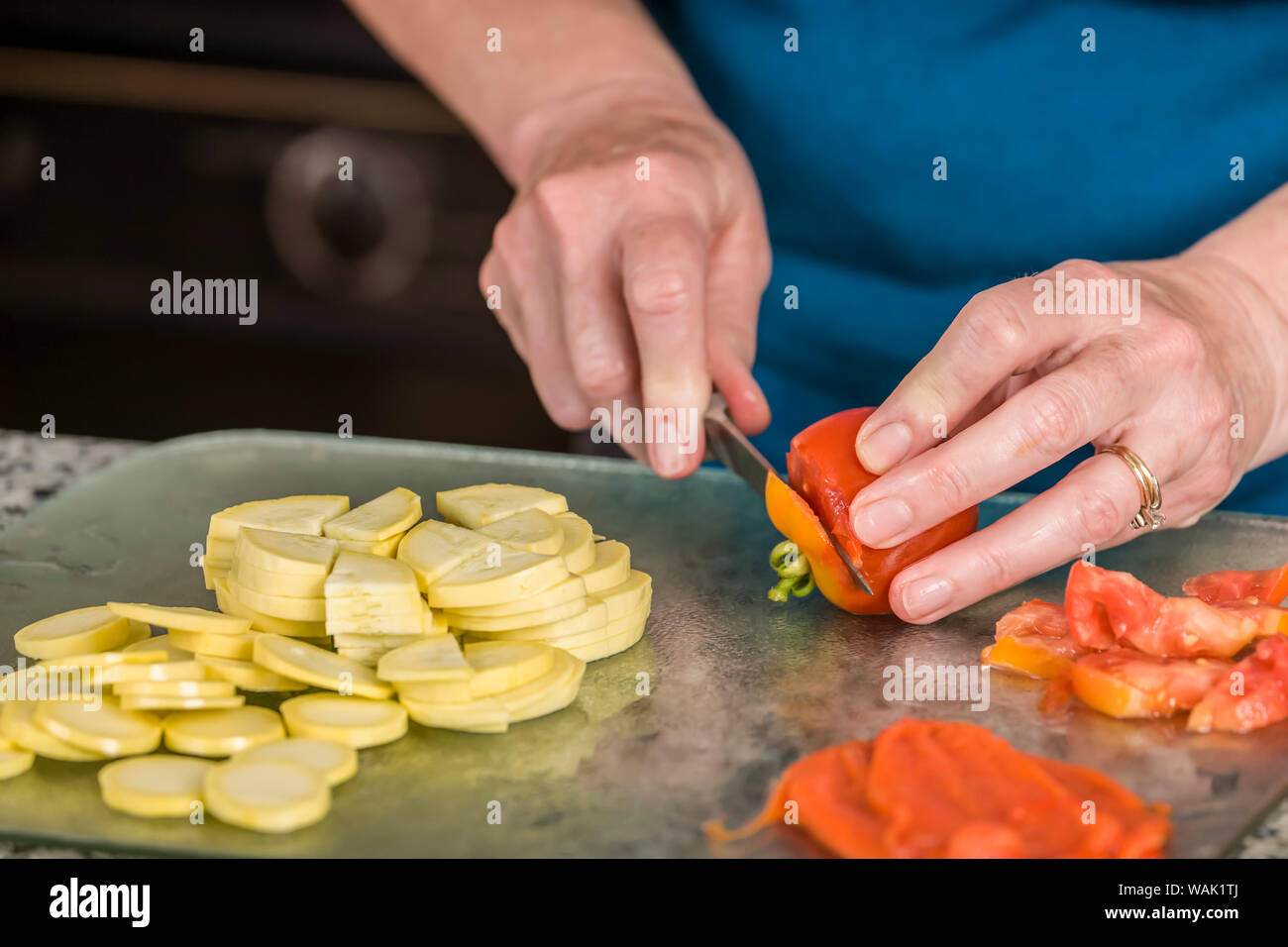 La donna per affettare il pomodoro. Veggie pizza condimenti mostrati sono stupice pomodoro, a fette estate squash e torrefatto pepe rosso. (MR) Foto Stock