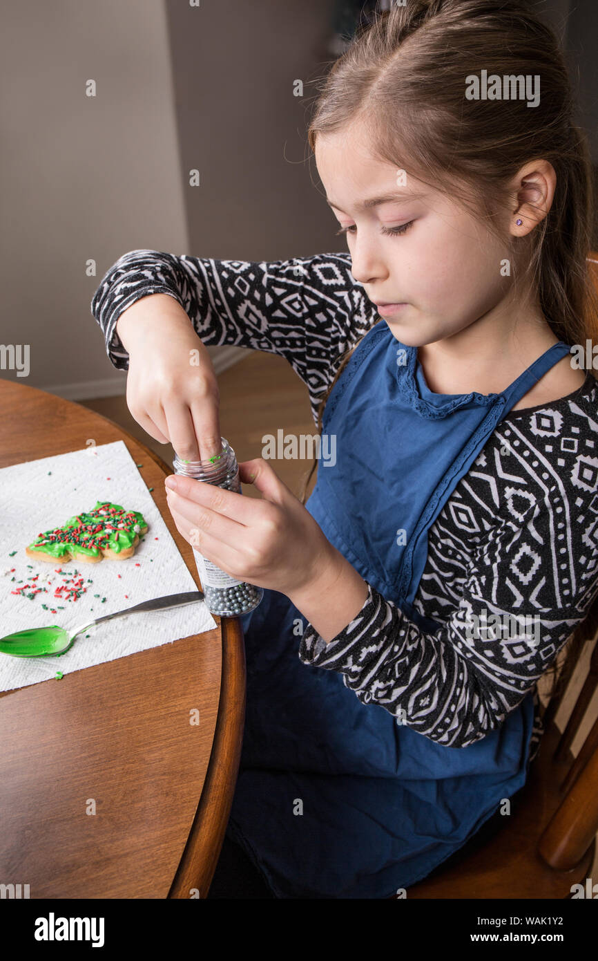 Ragazza di mettere lo zucchero silver pearl spruzza su di un albero di Natale di cookie di zucchero. (MR, PR) Foto Stock