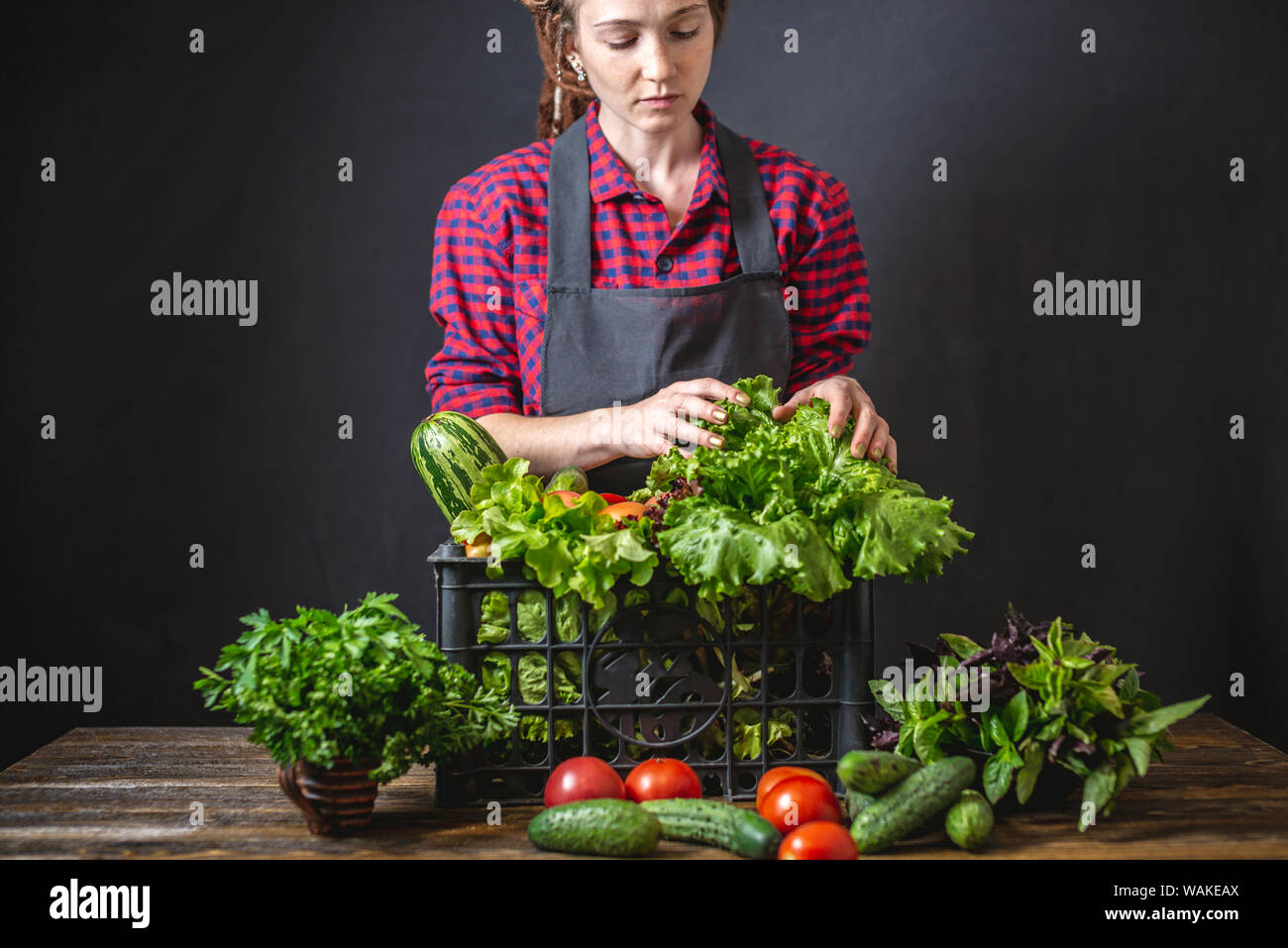 Un simpatico contadina è in possesso di una cassetta con verdura fresca e insalata verde su uno sfondo scuro. Materie organiche i prodotti coltivati in azienda. Foto Stock
