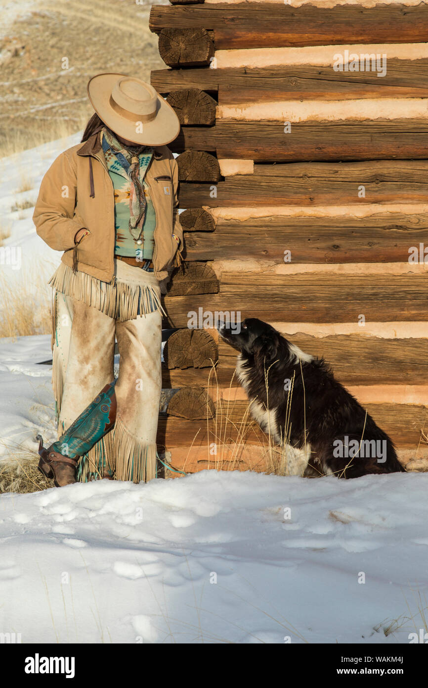 Cowboy a cavallo rigido sul nascondiglio Ranch, Shell, Wyoming. Cowgirl appoggiato log cabin con il suo ranch cane. (MR) Foto Stock