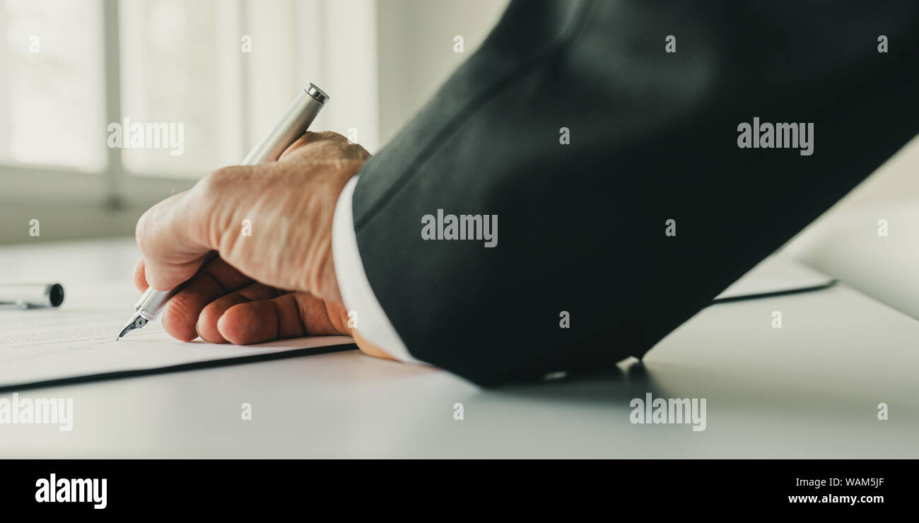 Angolo basso closeup vista di imprenditore firma un contratto sulla sua scrivania da ufficio luminose finestre. Foto Stock