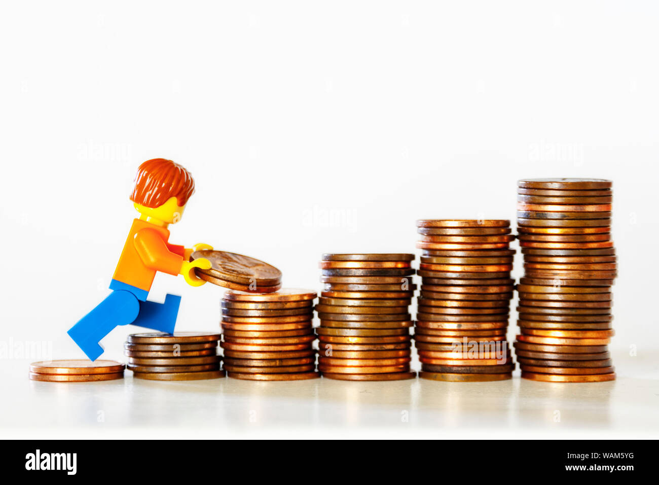 Concetto di risparmio di denaro - una figurina giocattolo che trasporta le monete su una pila di monete. Foto Stock