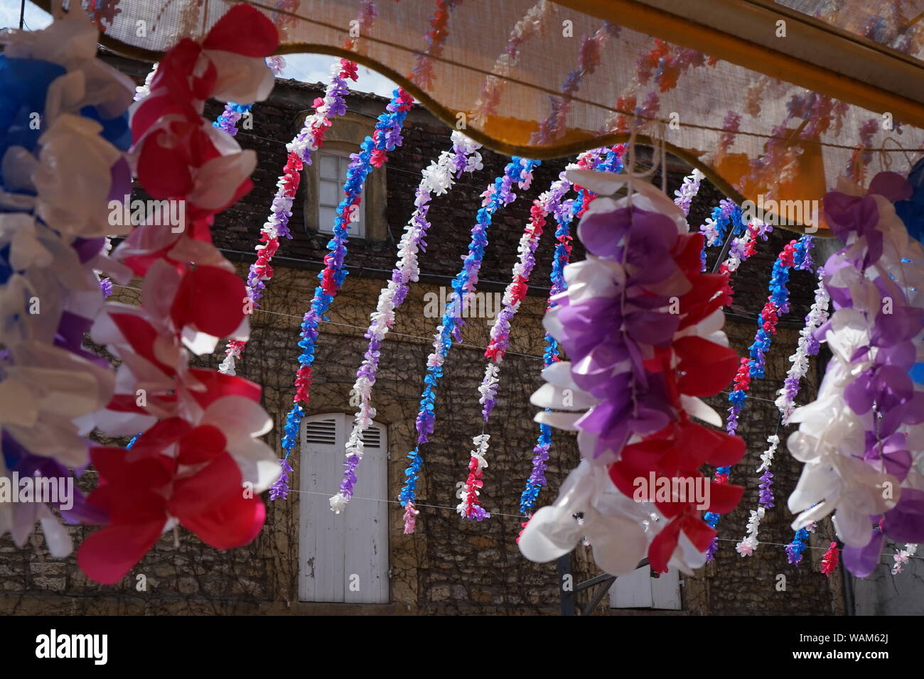 Una vista parziale di un tradizionale di pietra casa francese attraverso il festival dei fiori di Decorazioni da appendere una tenda shop Foto Stock