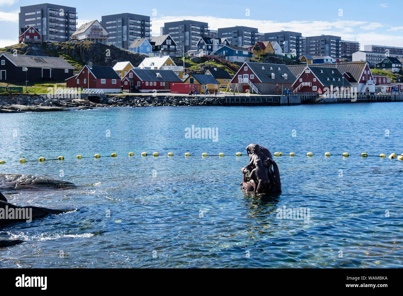 Scultura di Sedna, dea Inuit del mare circondato da acqua di mare nel porto coloniale (Kolonihavnen) con appartamenti moderni dietro. Nuuk Groenlandia Foto Stock