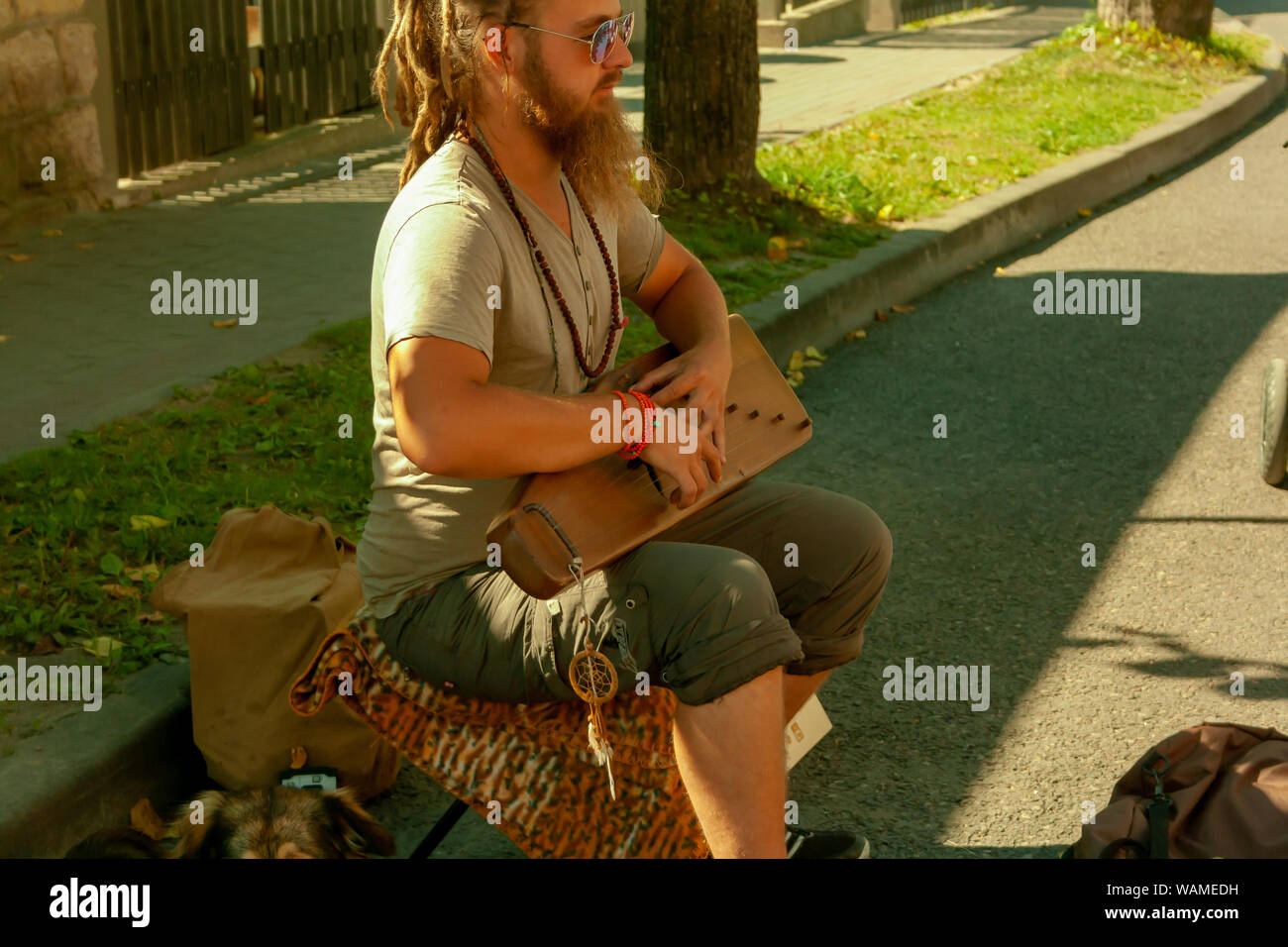 Cesis, Lettonia - Luglio 19, 2019: musicista di strada giocando il salterio mentre è seduto con un cane per strada in una giornata di sole. Foto Stock