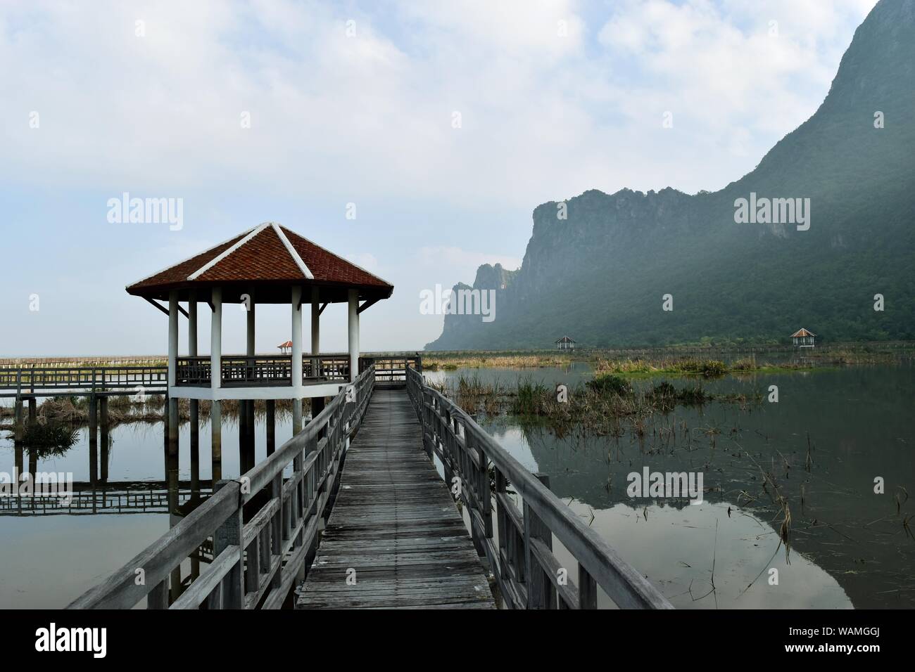 Khao Sam Roi Yot National Park, ponte di legno e il pavilion , Sun le riprese del fascio fuori da dietro la montagna di calcare riflessioni sul lago , della Thailandia Foto Stock