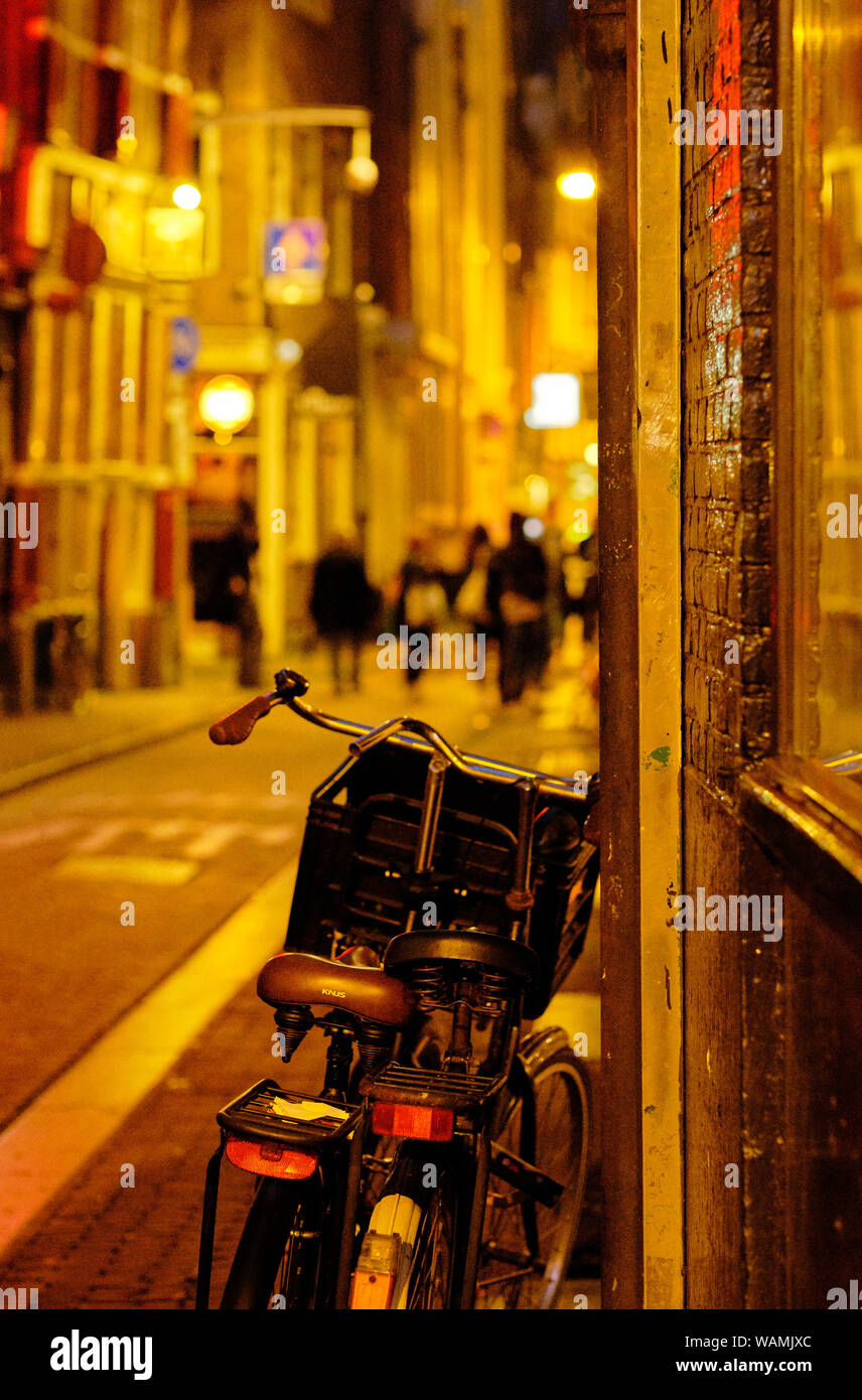 Le Biciclette parcheggiate e pedoni sulla stretta illuminata notte strade intorno al quartiere a luci rosse di Amsterdam Foto Stock