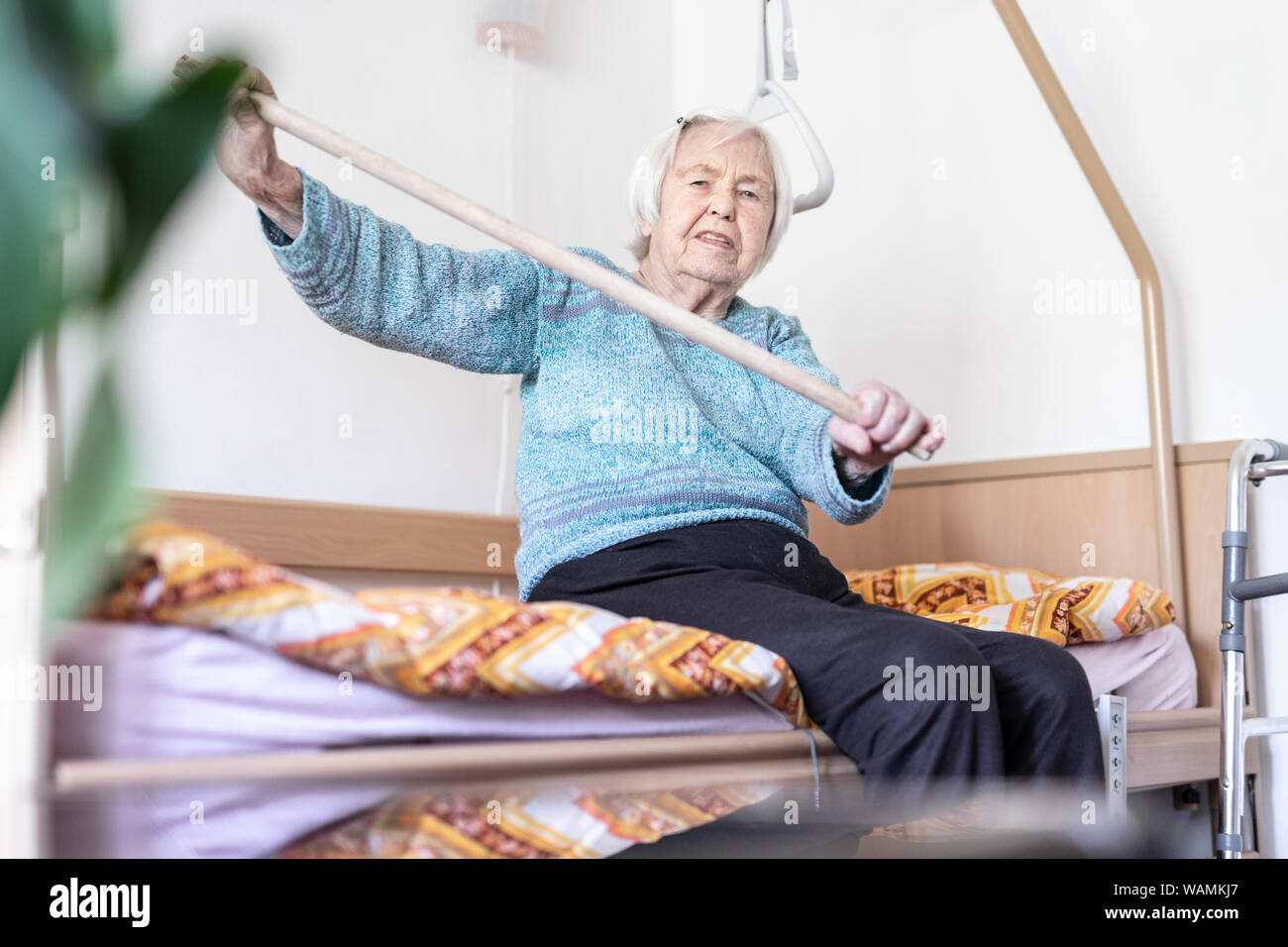 Anziani 96 anni vecchia donna esercizio con un bastone seduta sul suo cattivo. Foto Stock