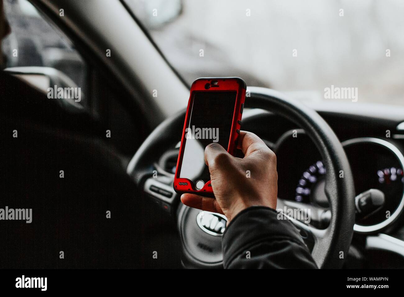 Una persona che tiene uno smartphone rosso seduto davanti al volante di un veicolo Foto Stock