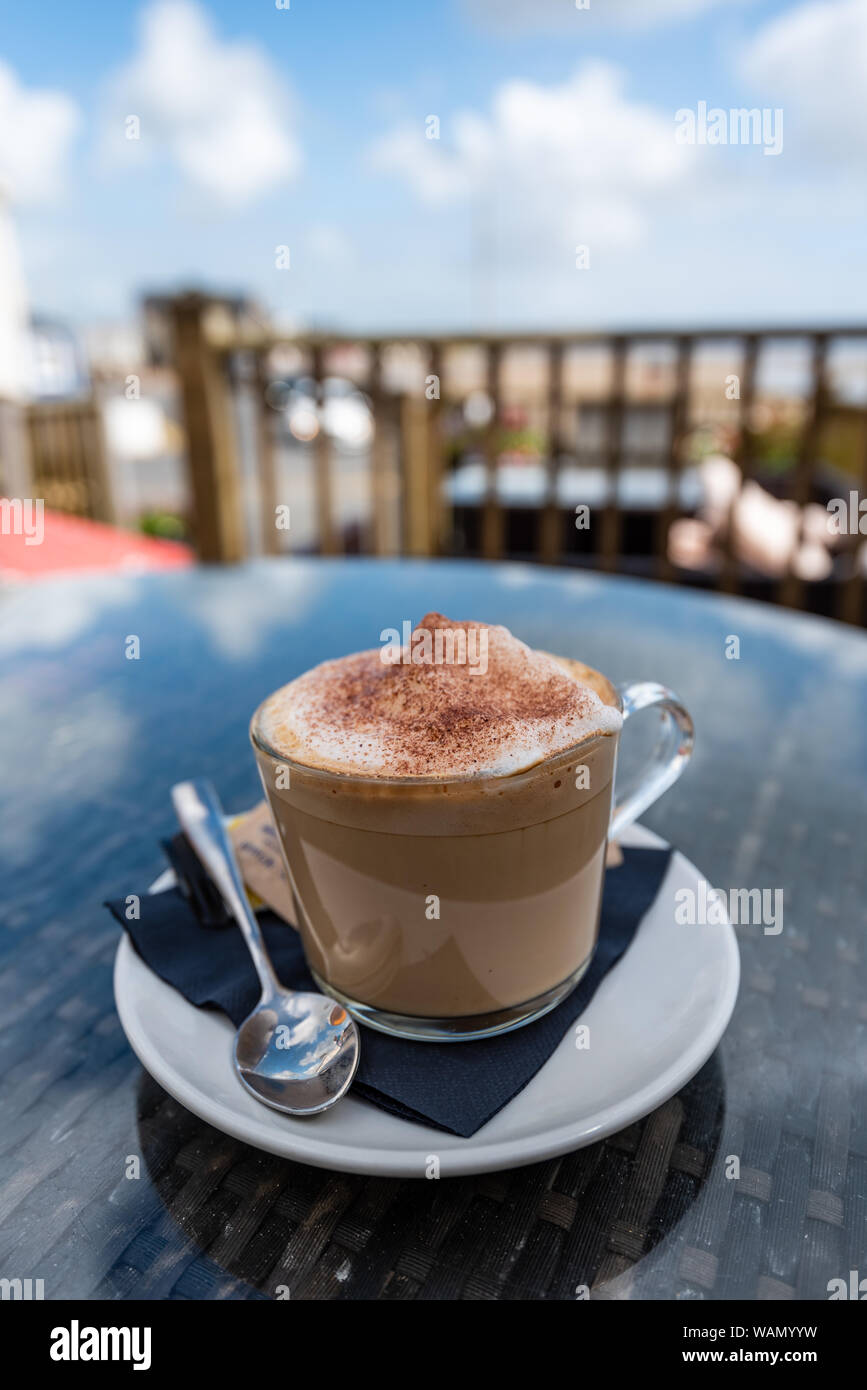 In prossimità di una tazza di caffè in una tazza di vetro al di fuori in un Regno Unito beach resort per vacanze Pendine Galles Foto Stock