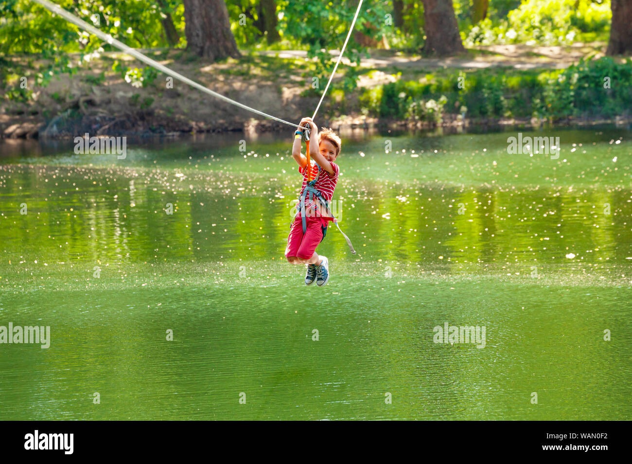 Felice ragazzo scivolare sulla linea di zip con il carrello sopra il lago Foto Stock