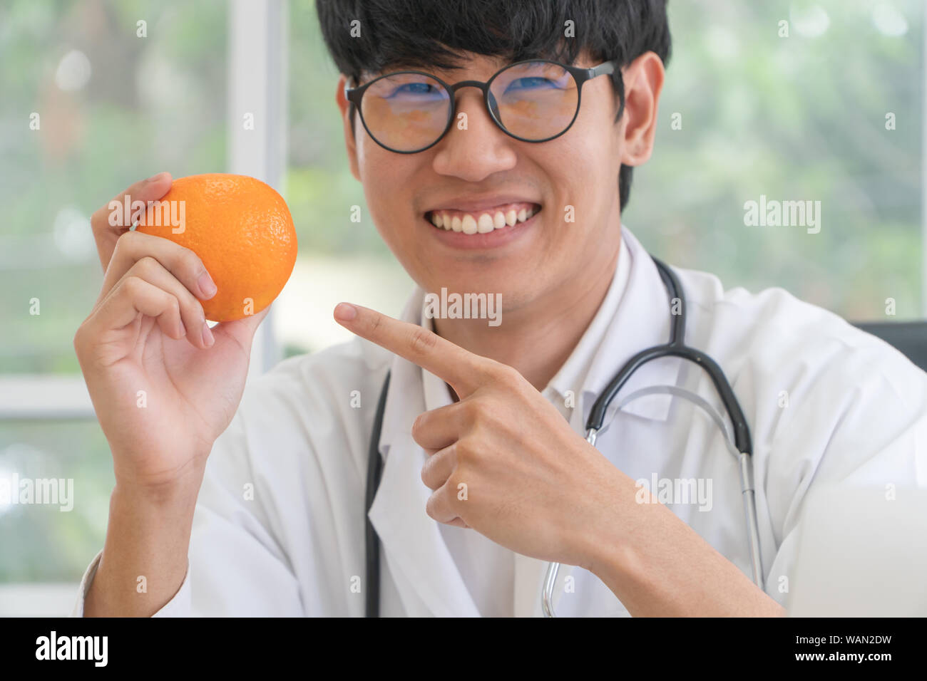 Medico nutrizionista o tenere premuto orange e puntare il dito all'arancione. in e sorriso in clinica. Dieta sana. Concetto di nutrizione il cibo come disposto Foto Stock