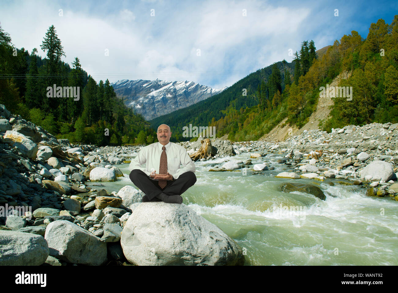 Uomo d'affari che pratica yoga seduto su una roccia in riva al fiume Beas, Manali, Himachal Pradesh, India Foto Stock