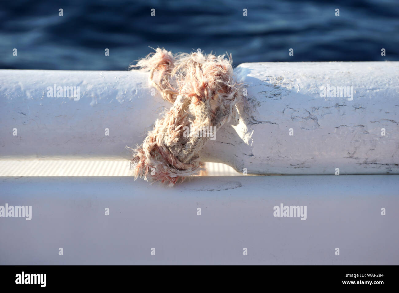 Fune spezzata legato con un nodo attorno a parte del vecchio pala in legno sulla barca bianca con mare blu superficie in background e spazio di copia Foto Stock
