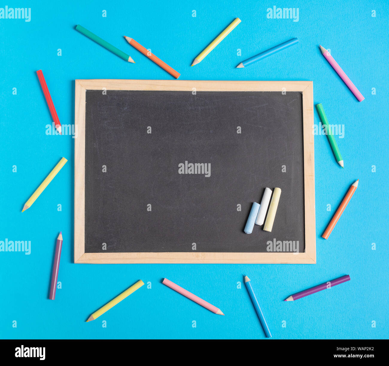 Lavagna vuota e matite colorate su uno sfondo blu. Si torna a scuola piana concetto laici Foto Stock