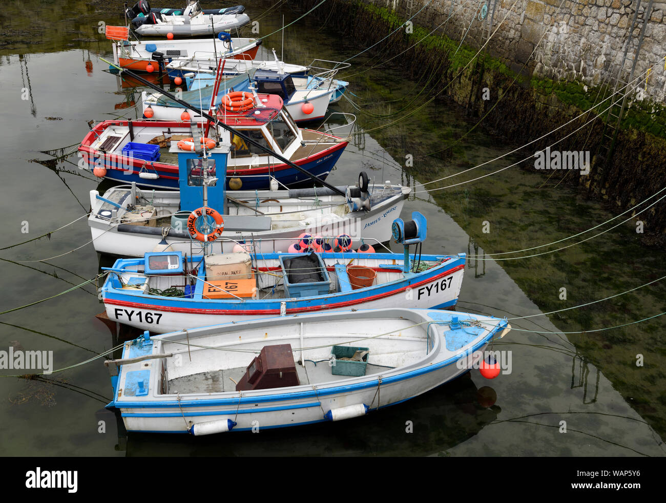 Fila di barche da pesca ormeggiate al molo di pietra di Porthleven Harbour a bassa marea Cornwall Inghilterra Foto Stock