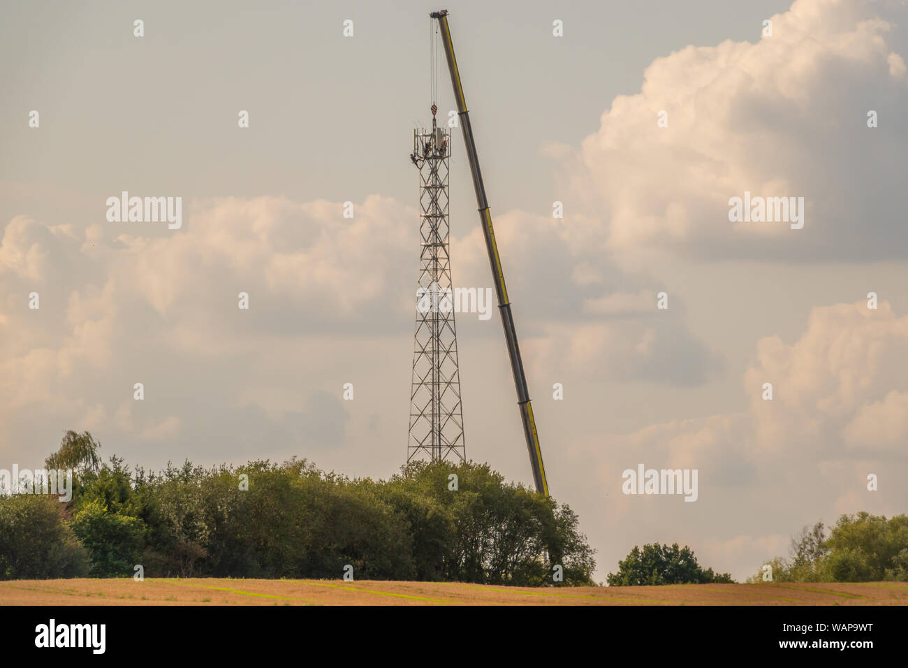 Un 5G torre di trasmissione è eretta su un campo con l aiuto di un enorme gru Foto Stock