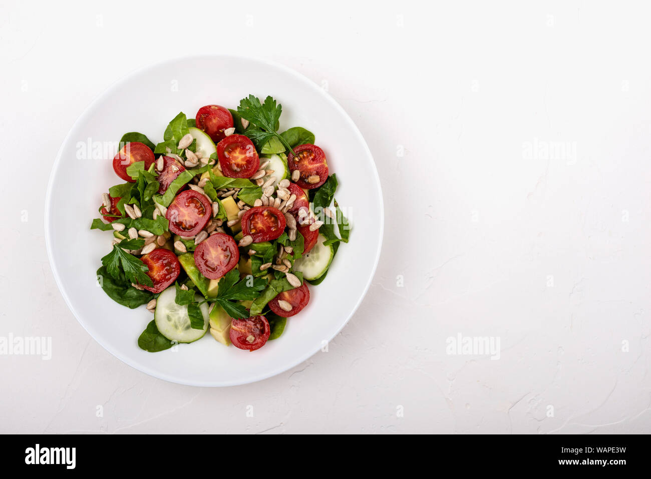 Con insalata di avocado, cetrioli e pomodori ciliegini, spinaci foglie di prezzemolo e i semi su una piastra bianca su sfondo bianco. Copia dello spazio. Foto Stock