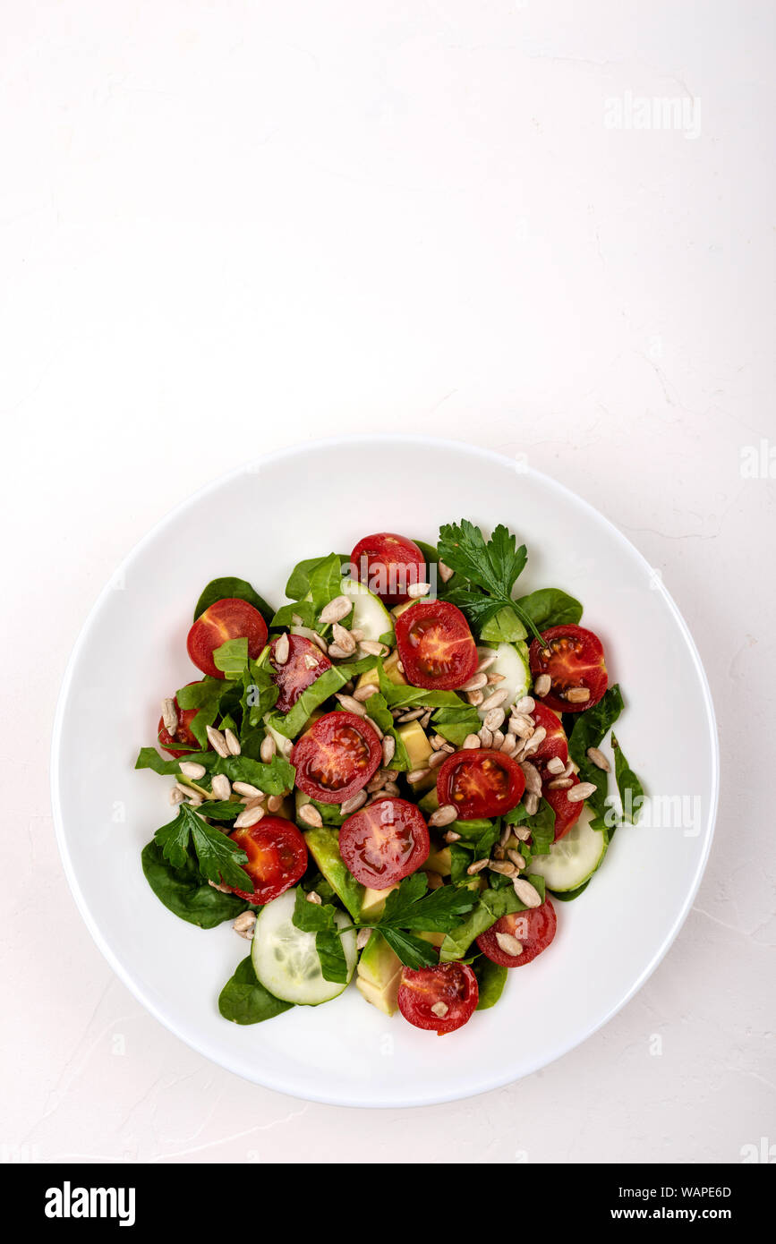 Con insalata di avocado, cetrioli e pomodori ciliegini, spinaci foglie di prezzemolo e i semi su una piastra bianca su sfondo bianco. Copia dello spazio. Foto Stock