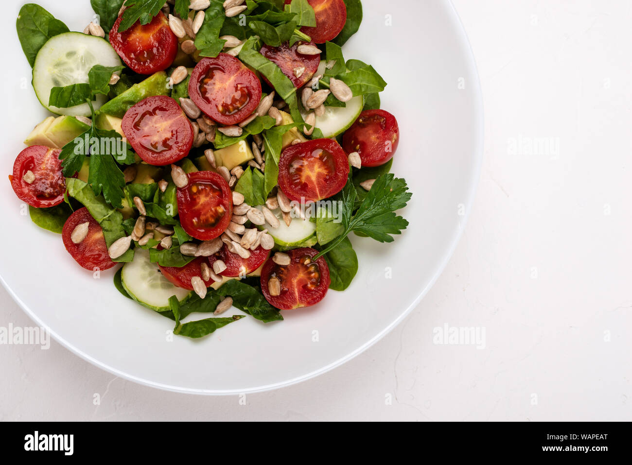 Con insalata di avocado, cetrioli e pomodori ciliegini, spinaci foglie di prezzemolo e i semi su una piastra bianca su sfondo bianco. Una sana alimentazione vegetariana. Foto Stock