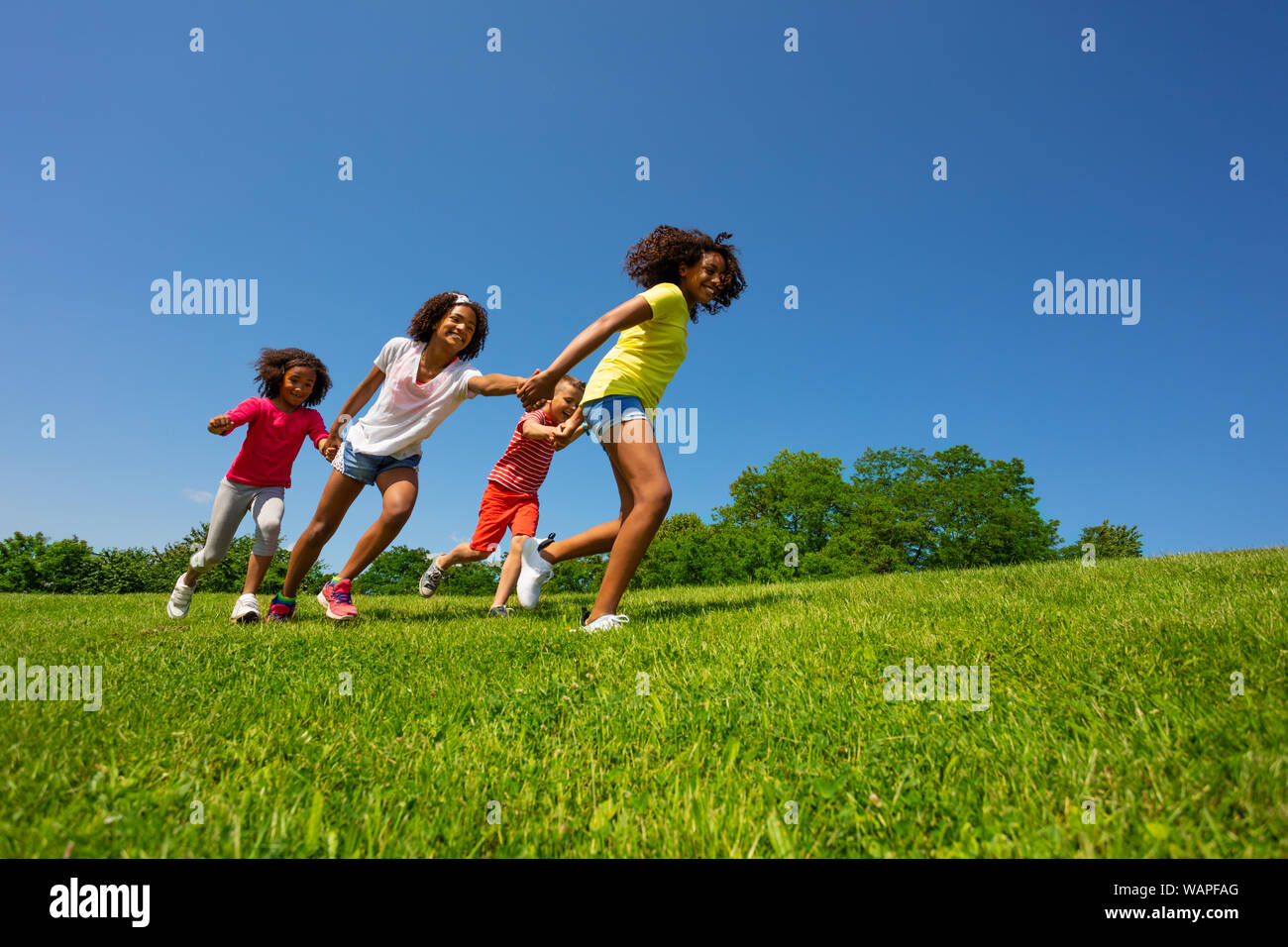 Ragazzo e ragazze correre veloce tenendo le mani sulla giornata di sole Foto Stock