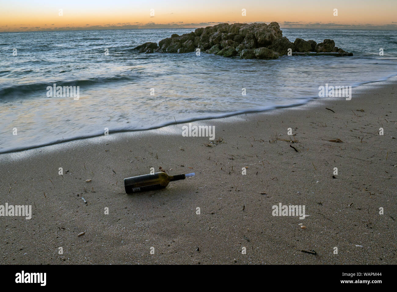 Bottiglia di vino con un arrotolato pezzo di carta lavato fino ad una spiaggia di sabbia. Foto Stock
