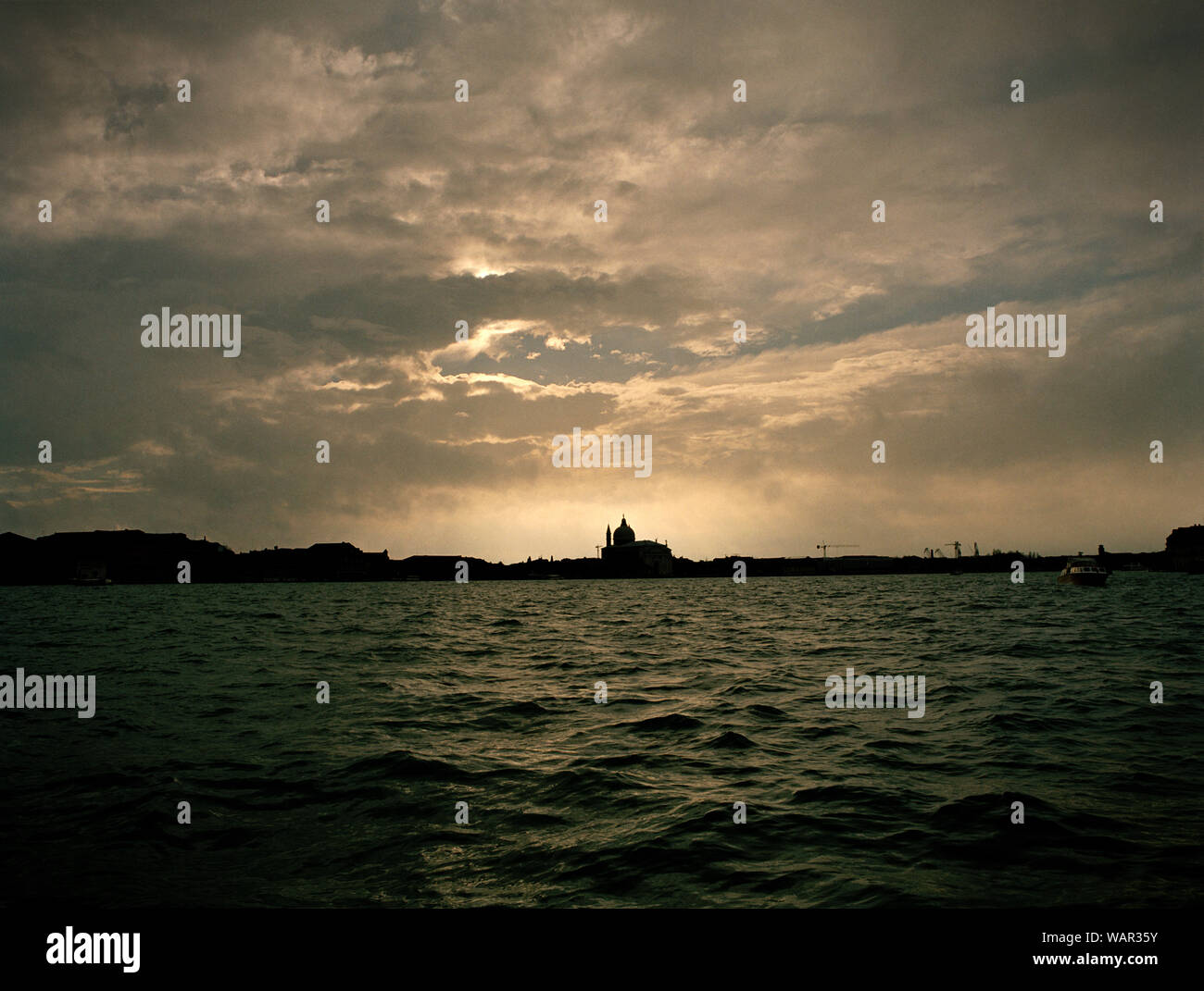 Vista del sole che splende attraverso un cielo nuvoloso sopra l'acqua. Foto Stock