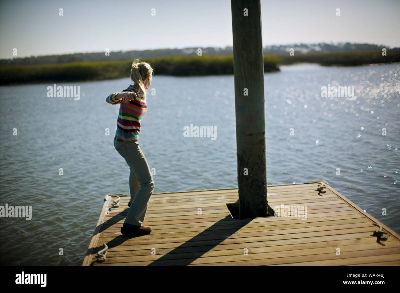 Ragazza adolescente scrematura di rocce di acqua mentre in piedi sull'estremità di un molo. Foto Stock